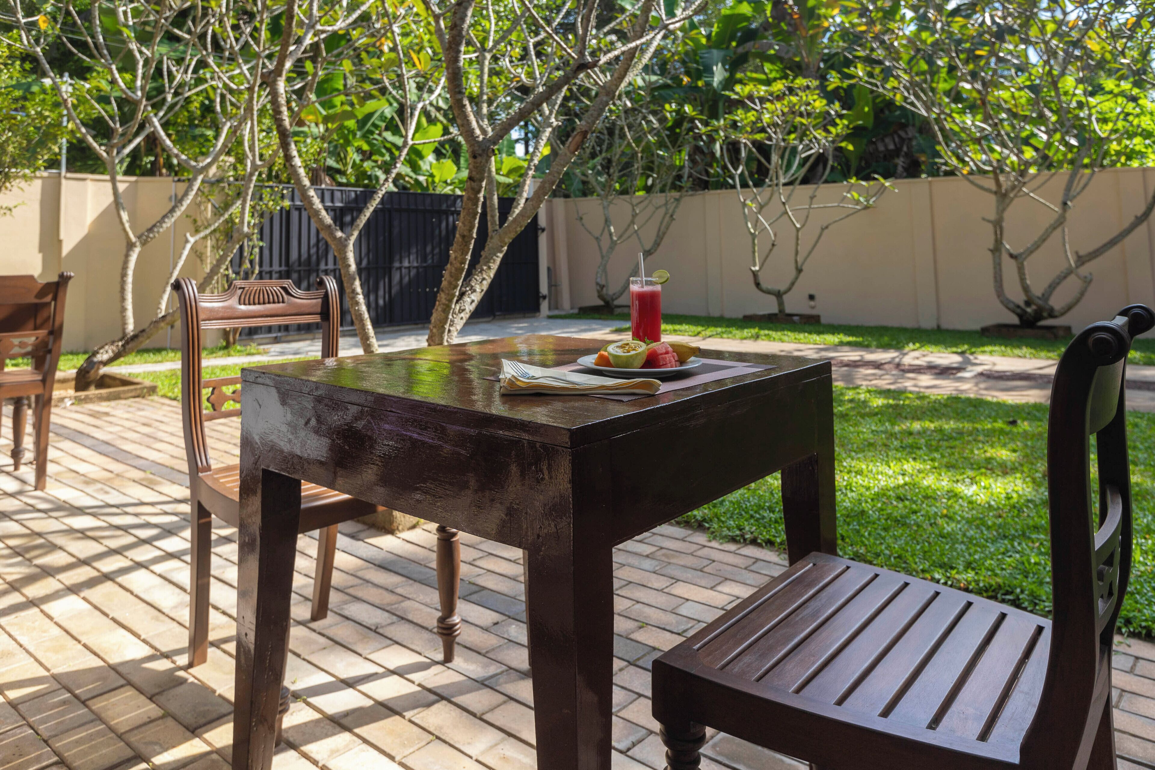 An outdoor patio with a wooden table, chairs, and a drink with fruit.