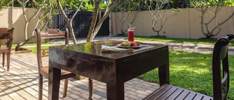 An outdoor patio with a wooden table, chairs, and a drink with fruit.