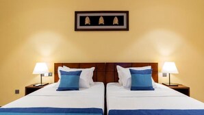 Cama doble con ropa de cama blanca y azul, dos lámparas de noche y un cuadro enmarcado sobre la cama.