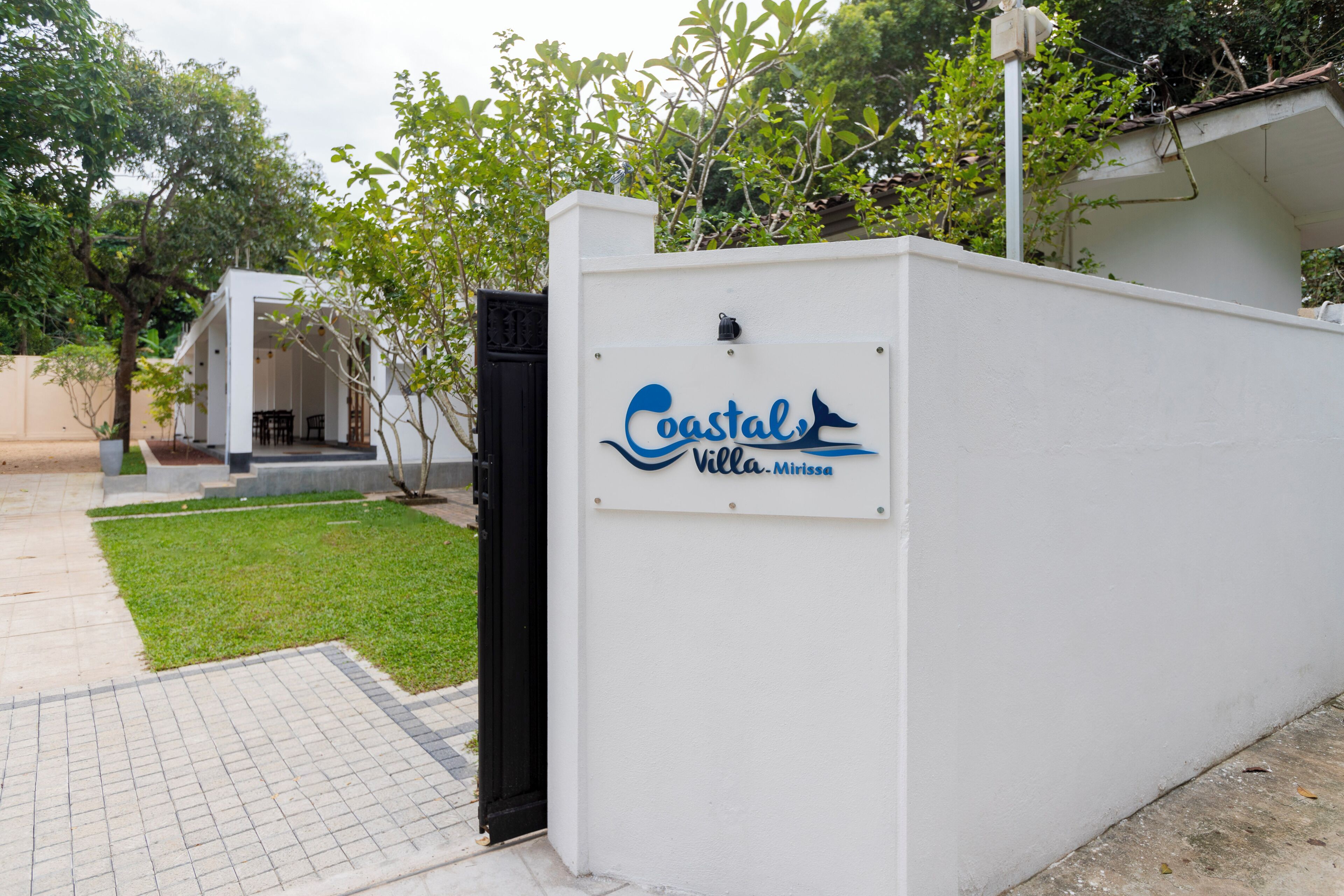 Un mur blanc avec une enseigne indiquant « Castal Villa-Mirissa » et un portail noir.