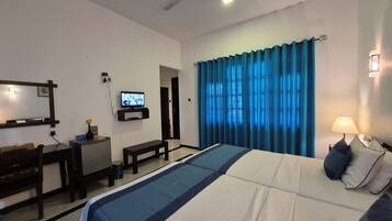 Habitación de hotel con cama, escritorio, televisión, ventilador de techo y ventana con cortinas.