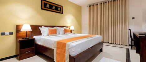 A hotel room with a bed, bedside tables, a desk, and a window with curtains.