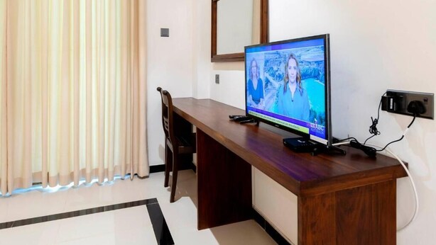Una habitación con escritorio de madera, televisor, silla y ventana con cortinas.