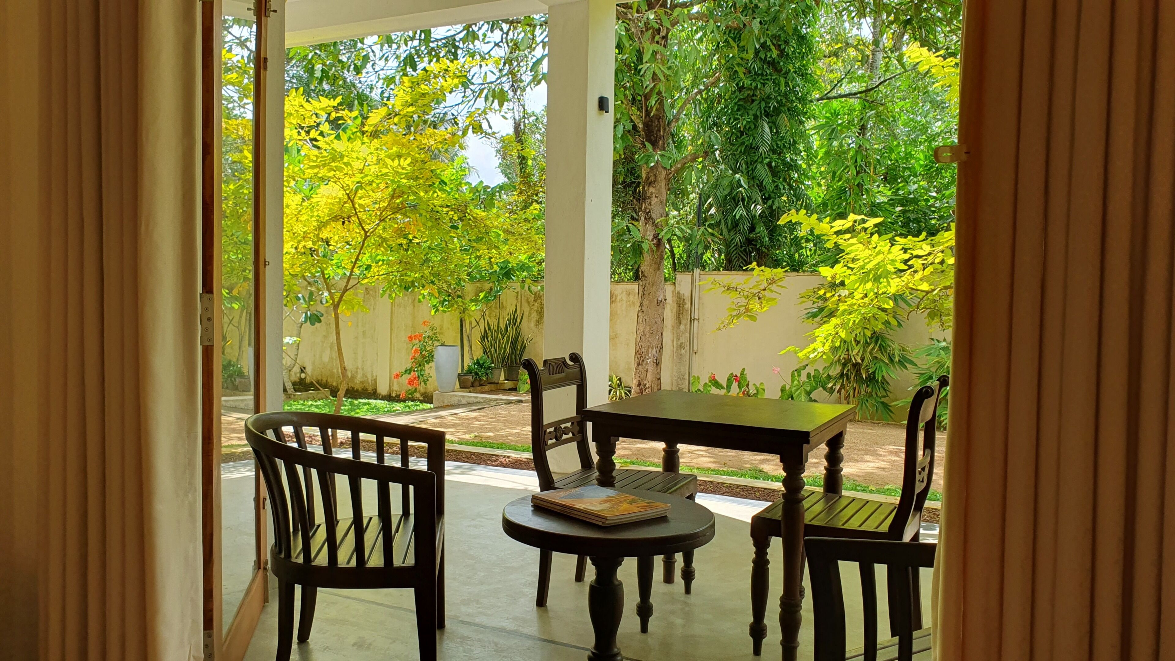 Une terrasse extérieure avec une table et des chaises, entourée de verdure et d’un mur blanc.