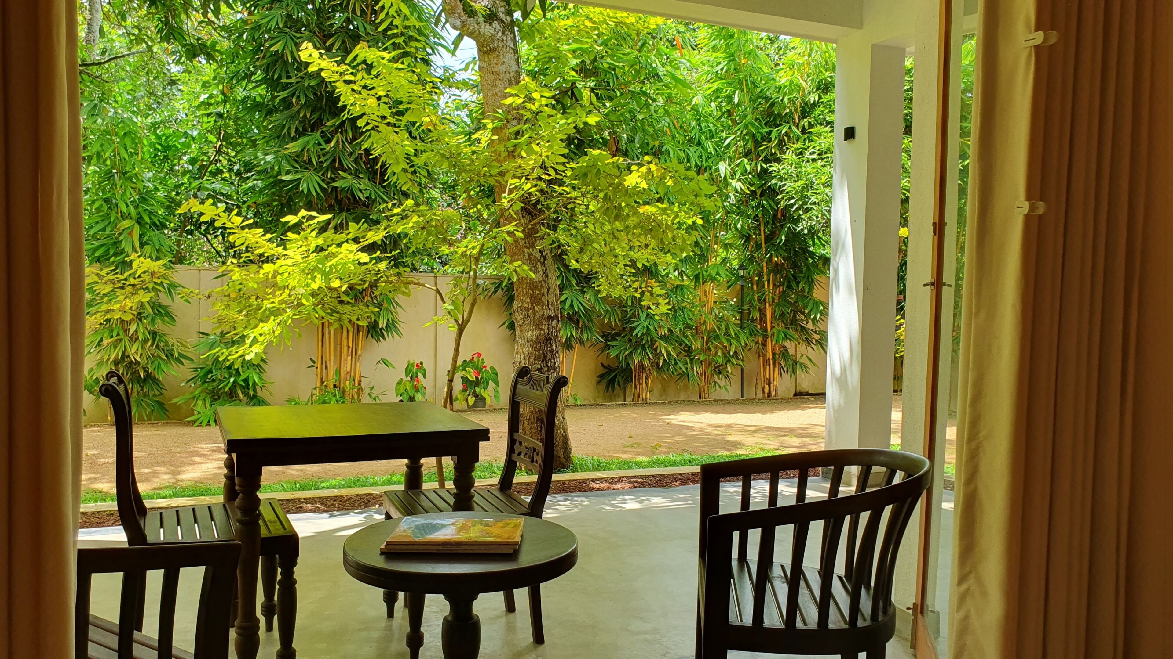 An outdoor seating area with a table and chairs, surrounded by lush greenery and trees.