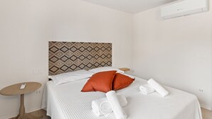 Una habitación de hotel con cama, cabecera estampada, una mesita redonda y aire acondicionado instalado en la pared.