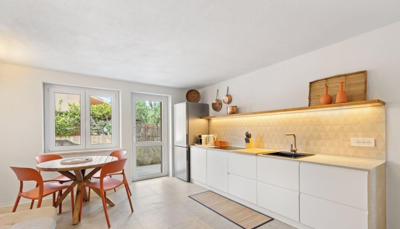 Una cucina moderna con mobili bianchi, un tavolo da pranzo in legno e sedie, e una vista attraverso la porta in vetro.