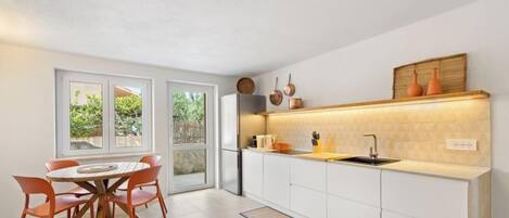 Una cucina moderna con mobili bianchi, un tavolo da pranzo in legno e sedie, e una vista attraverso la porta in vetro.