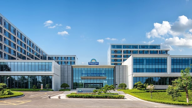 Un hotel moderno con fachada de vidrio, señalización de Days Inn y una entrada ajardinada.