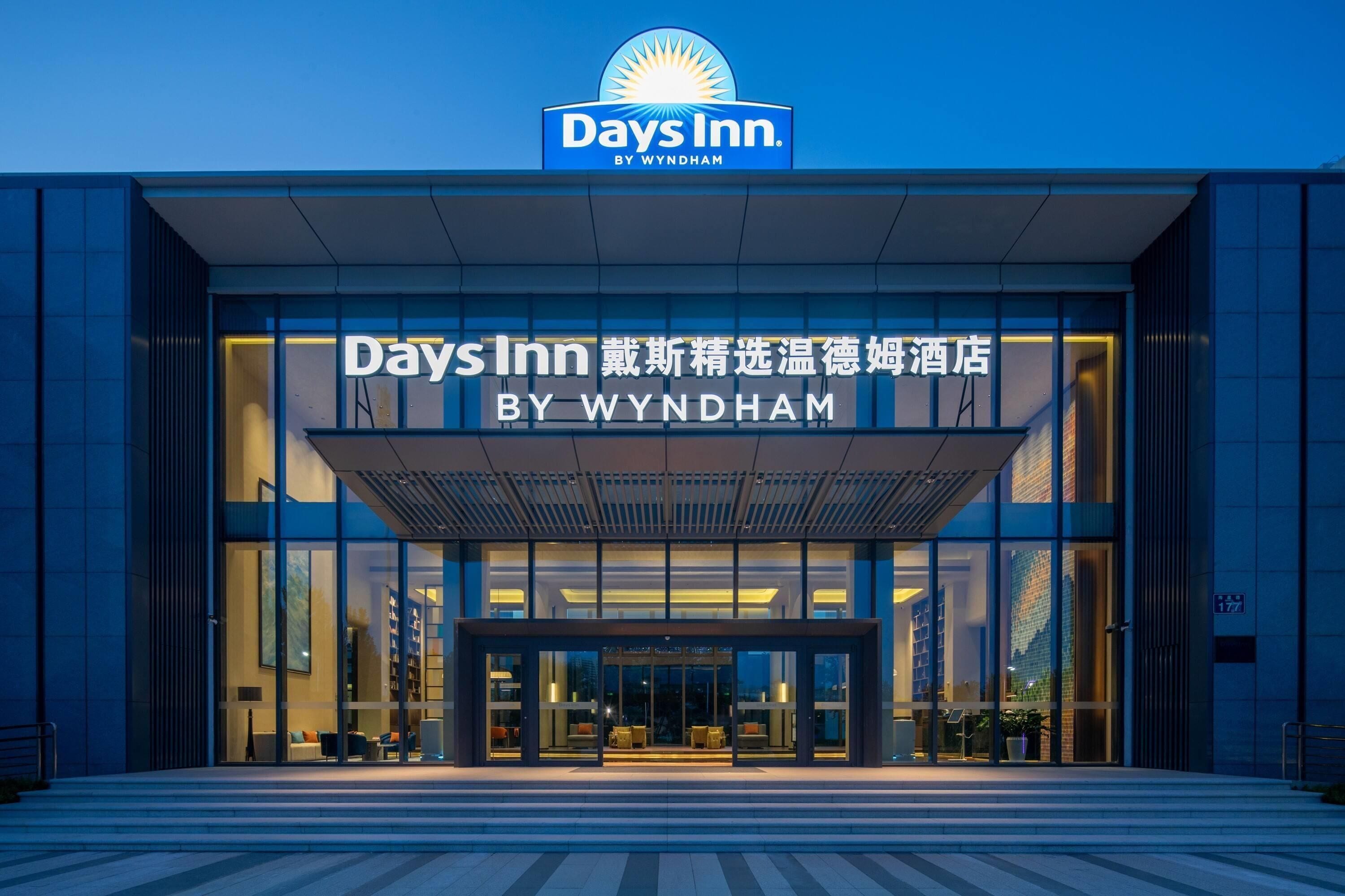 A Days Inn by Wyndham hotel entrance with a modern design, large glass windows, and a clear sky.