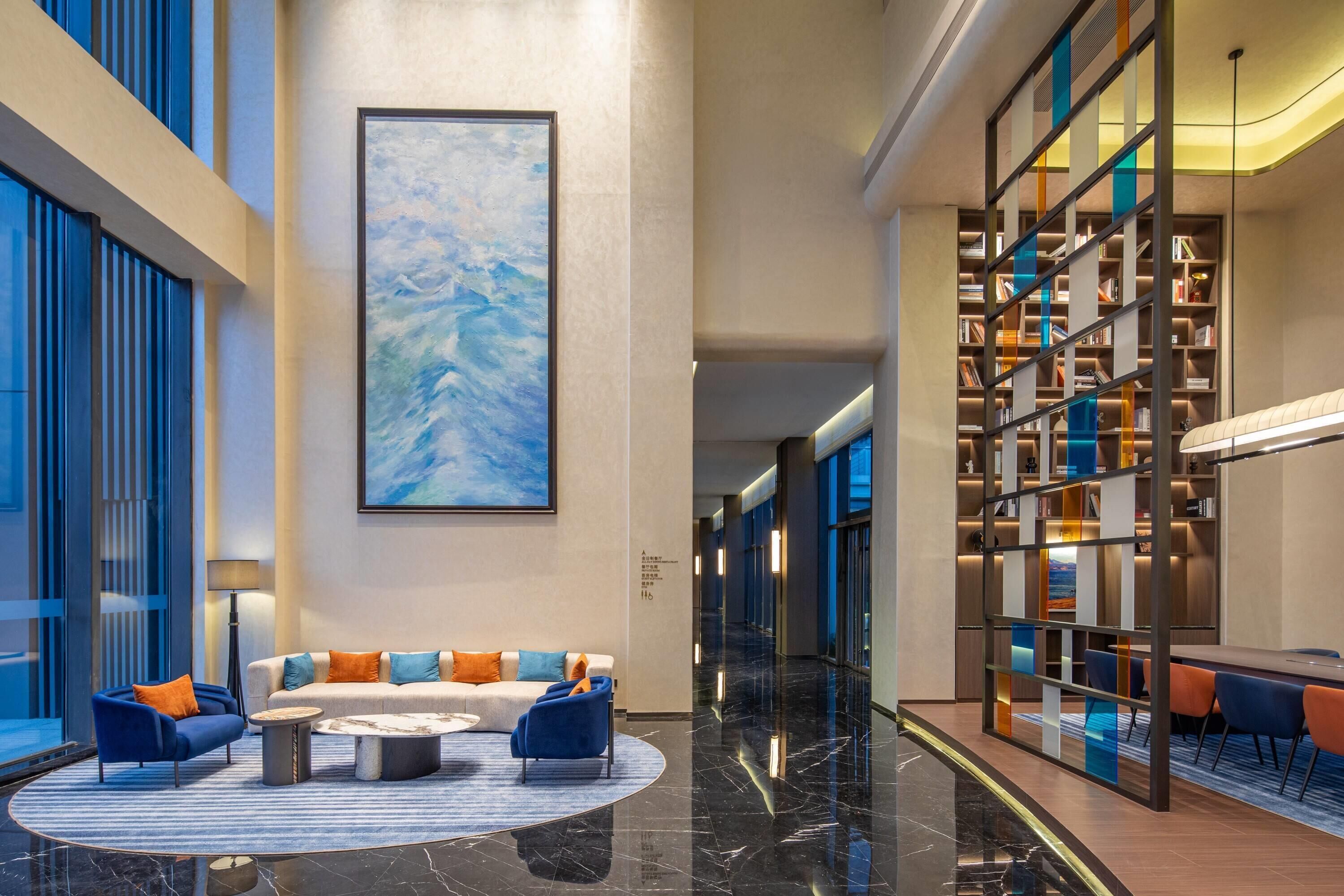 A modern lobby with a seating area, a large abstract painting, and a well-lit bookshelf.