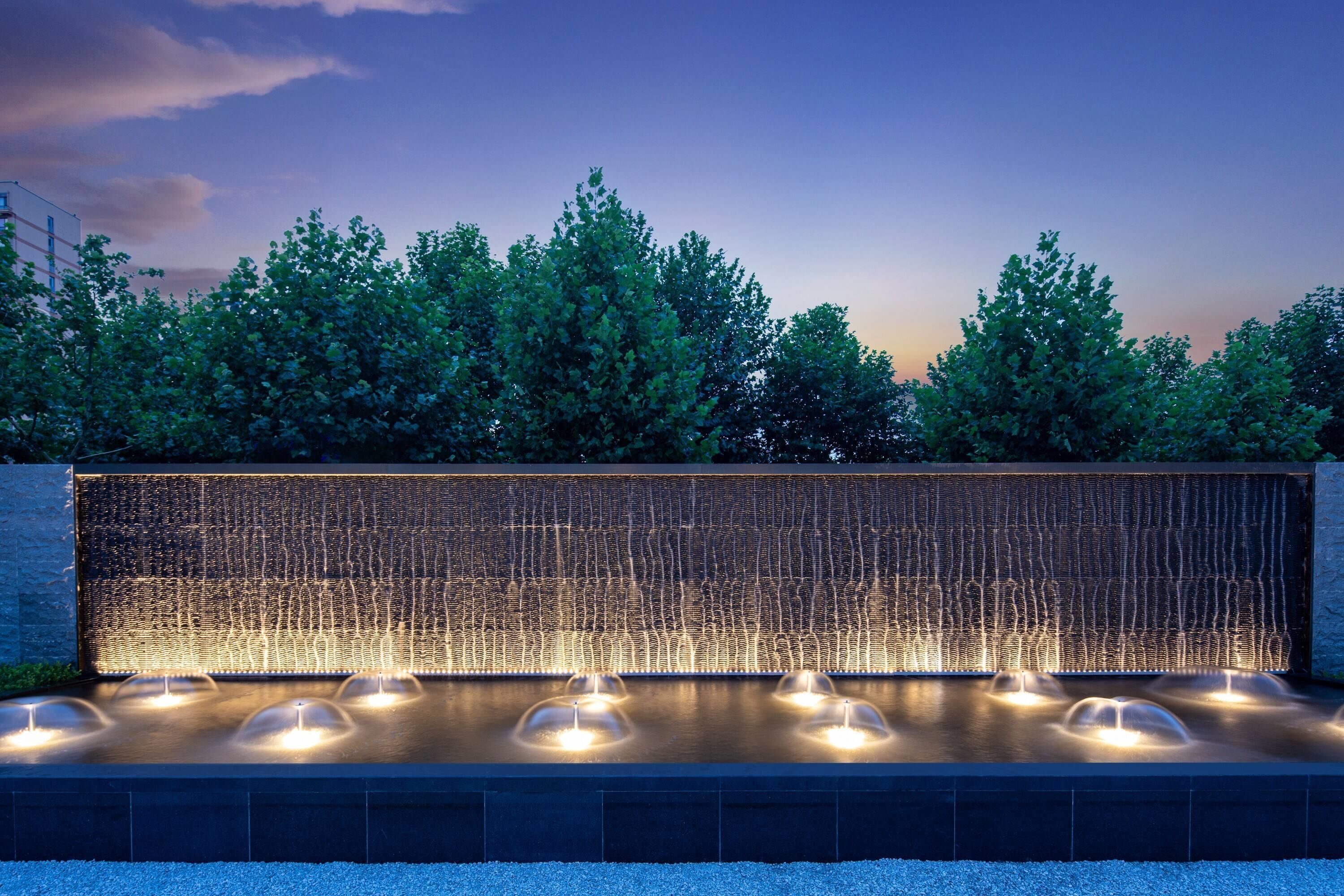 A water feature with multiple fountains and a wall with vertical lines.