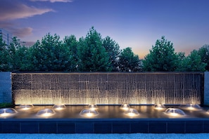 A water feature with multiple fountains and a wall with vertical lines.