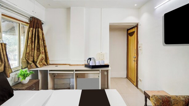 Une chambre d’hôtel avec un lit, un bureau doté d’une bouilloire, une plante en pot et un téléviseur fixé au mur.