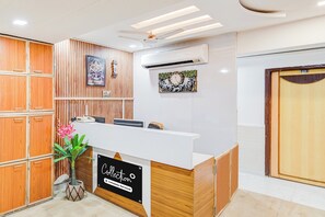 A reception area with a wooden panel wall, a reception desk, and a wall-mounted clock. - Collection O Maninagar East (Ahmedabad)
