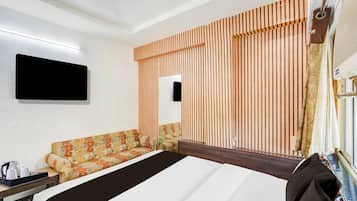 Une chambre d’hôtel comprenant un lit, un canapé, un téléviseur à écran plat fixé au mur et une fenêtre avec des rideaux.