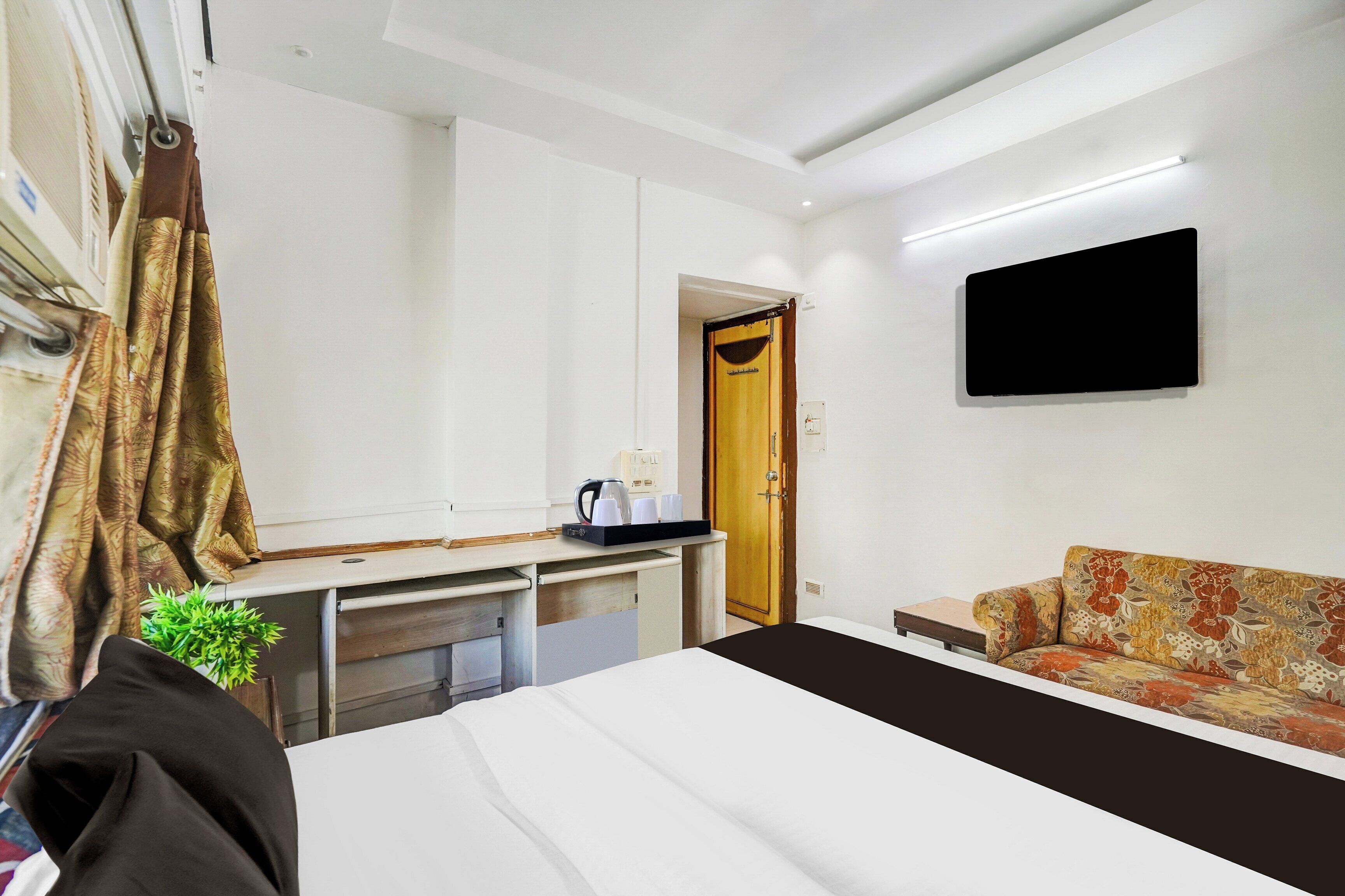 Quarto de hotel com cama, escrivaninha, sofá, televisão de tela plana, porta e janela.