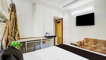 Quarto de hotel com cama, escrivaninha, sofá, televisão de tela plana, porta e janela.