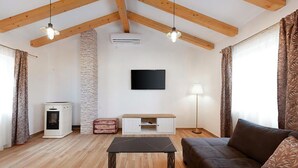 En stue med træloft, et fladskærms-tv monteret på væggen, et hvidt tv-møbel, en brun sofa, et lille bord og en lampe.
