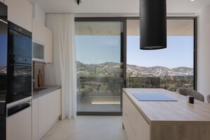A modern kitchen with a large window, a view of a hilly landscape, and a dining area with a table and chairs. - Gaia Villas - With 2 Private Pools (Bali)