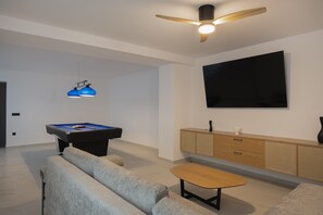 A modern living room with a pool table, a ceiling fan, a flat-screen TV, and a sofa. - Gaia Villas - With 2 Private Pools (Bali)