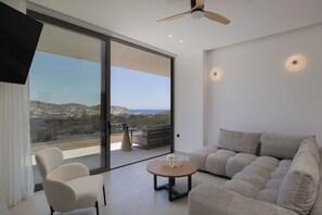 A modern living room with a sofa, chairs, a small table, and a TV mounted on the wall. - Gaia Villas - With 2 Private Pools (Bali)