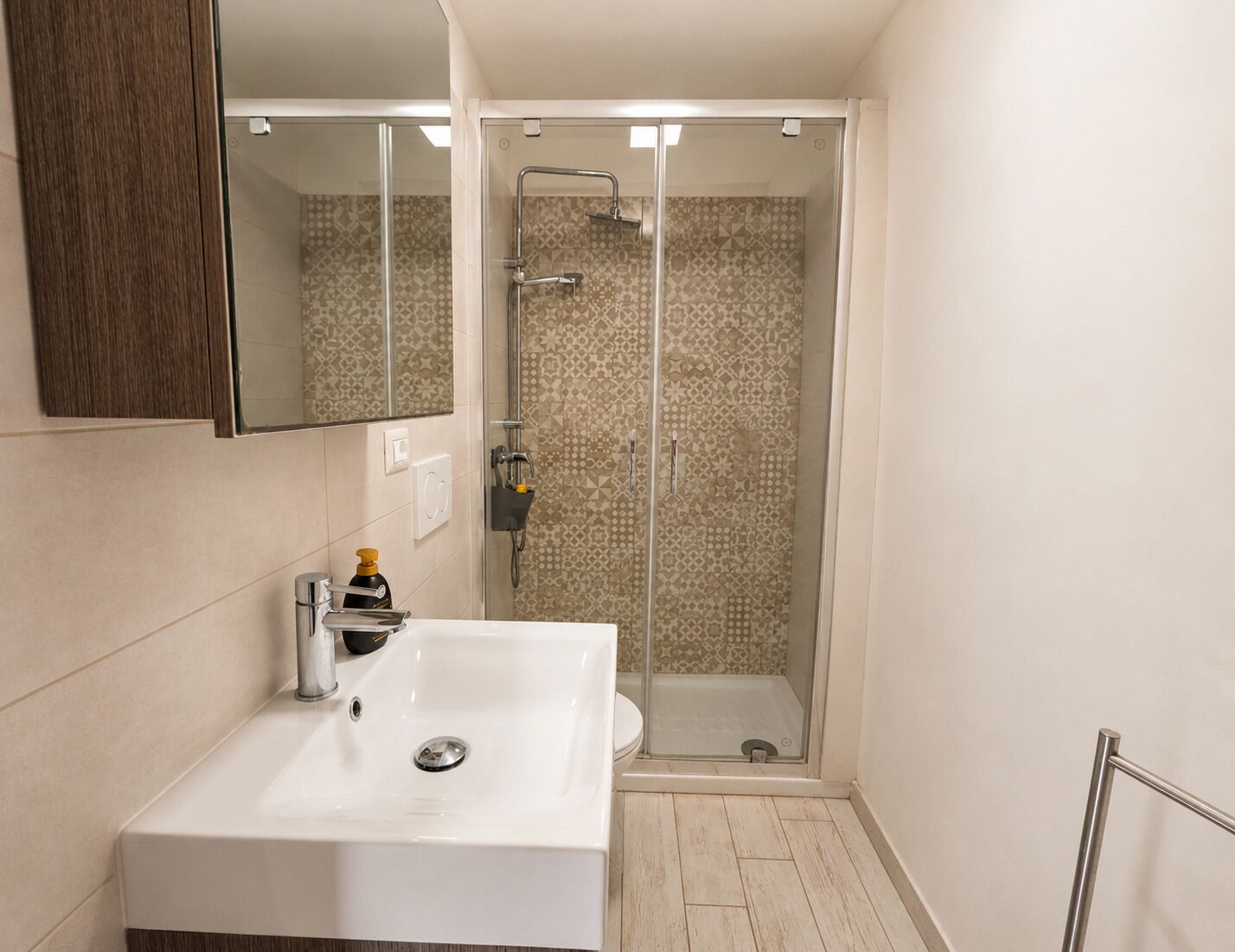 Un bagno moderno con un lavandino bianco, una cabina doccia in vetro e uno specchio sopra il lavandino.