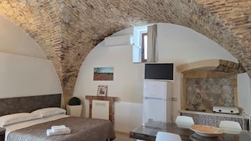 Ein Zimmer mit einem Bett, einem kleinen Tisch, einem Fernseher und einer Küchenzeile mit einer Steinwand.