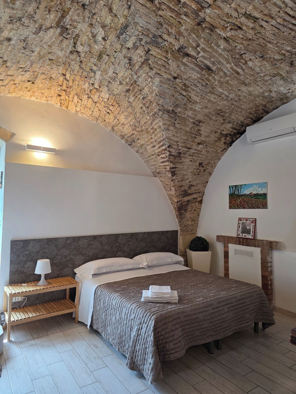 A bedroom with a stone ceiling, a bed with a striped bedspread, a bedside table with a lamp, and a framed picture on the wall.