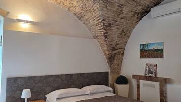 A bedroom with a stone ceiling, a bed with a striped bedspread, a bedside table with a lamp, and a framed picture on the wall.