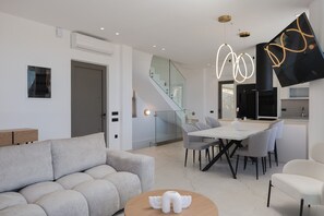 A modern living room with a sofa, a dining table with chairs, a kitchen area, and a staircase. - Luxurious Villa Artemis - With Private Pool (Bali)