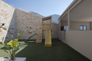 Ein Kinderspielbereich mit Rutsche und Klettergerüst, umgeben von einer Steinmauer und einem Gebäude.