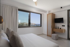 A modern bedroom with a large bed, a TV mounted on the wall, and a view of the sea through a large window. - Luxurious Villa Artemis - With Private Pool (Bali)
