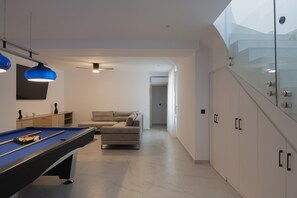 Ein modernes Wohnzimmer mit Billardtisch, einer Couch und einer Vitrine.