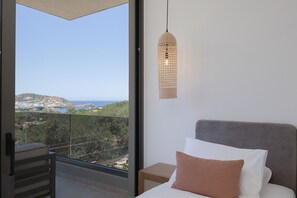 Ein Schlafzimmer mit einem Bett, einem Nachttisch, einer Pendelleuchte und Blick auf eine Küstenlandschaft.