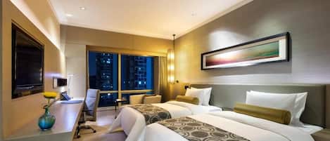 A hotel room with two beds, a desk, a chair, a TV, and a window with a night view.