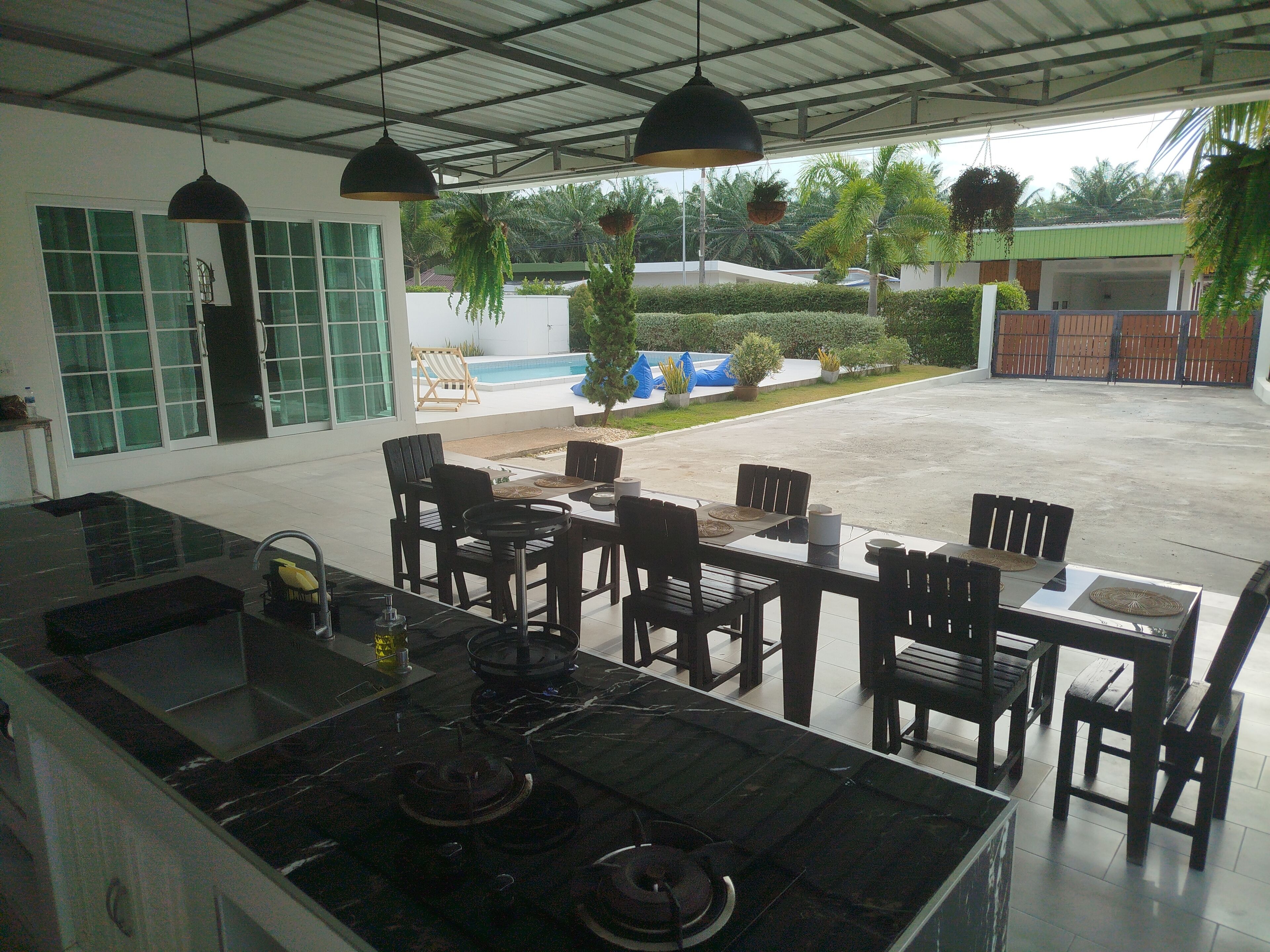A modern kitchen with a central island, dining area with chairs, and a view of a swimming pool and greenery.