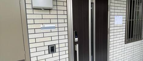 A building entrance with a numbered door, a security camera, and a light fixture.