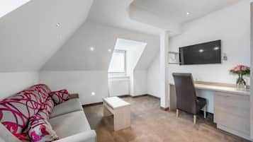 A modern loft bedroom with a sloped ceiling, a large window, a flat-screen TV, a desk, and a sofa.