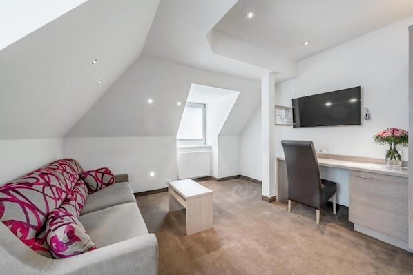 A modern loft bedroom with a sloped ceiling, a large window, a flat-screen TV, a desk, and a sofa. - Hotel Garni Christine - Ischgl (Ischgl)