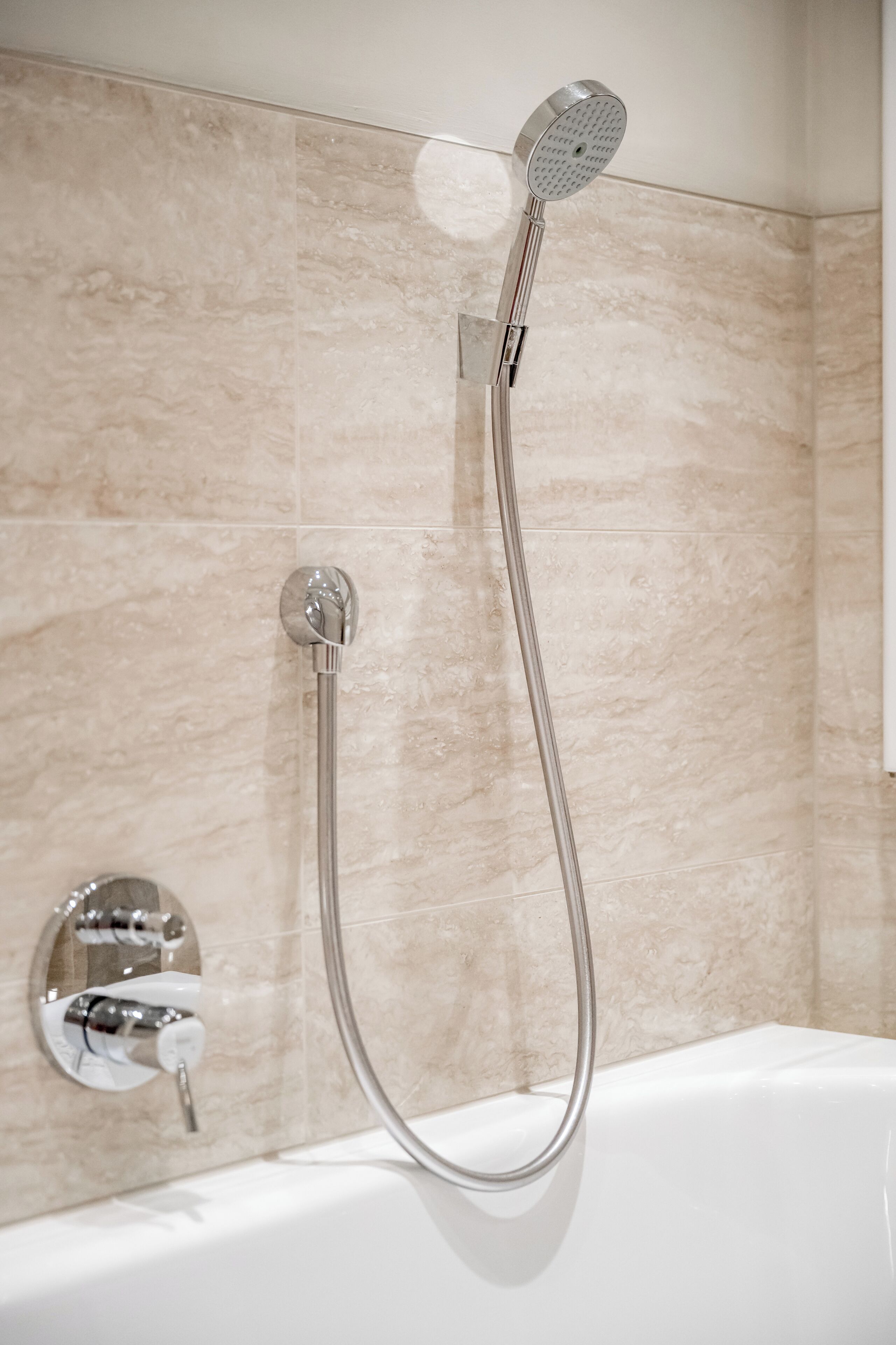 A bathroom with a shower head mounted on a wall, a handheld shower attachment, and a bathtub.