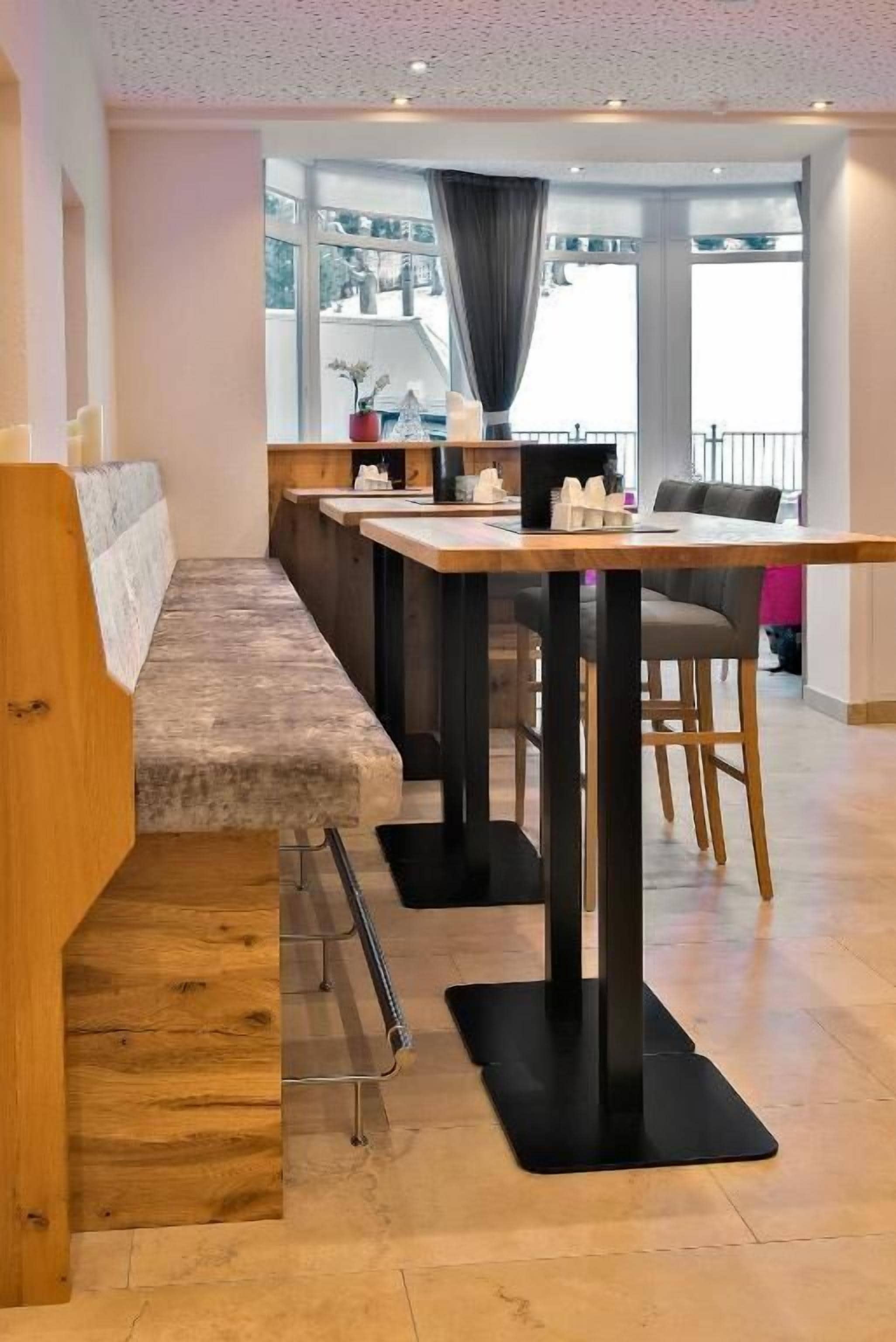 A modern interior with a long bench seating area, a wooden table, and a view through large windows.