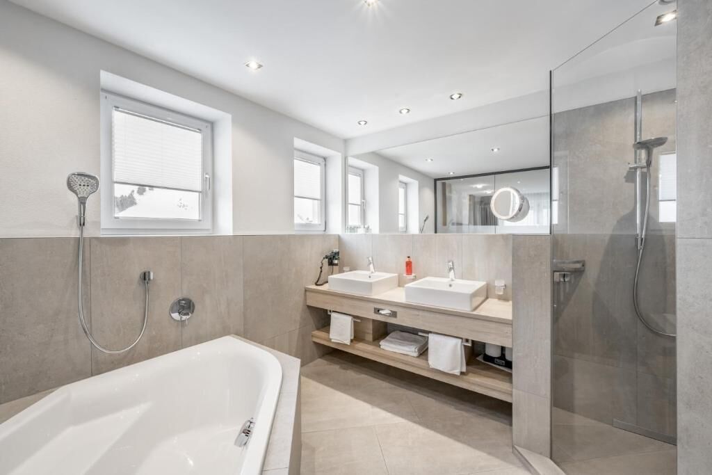 Un baño moderno con bañera, dos lavamanos, ducha y un espejo grande.