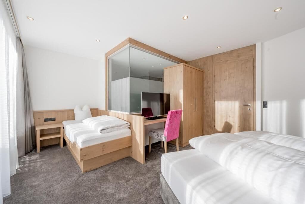 A hotel room with a bed, a desk, a chair, a wardrobe, and a large mirror.
