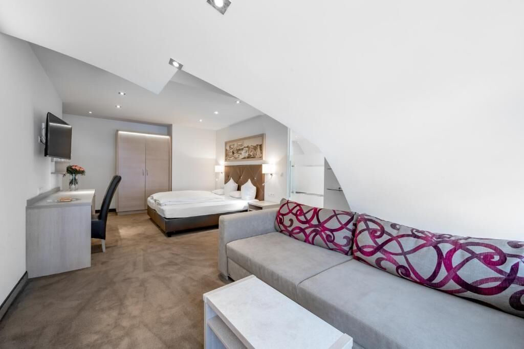 A modern bedroom with a bed, a sofa, a desk, and a TV.