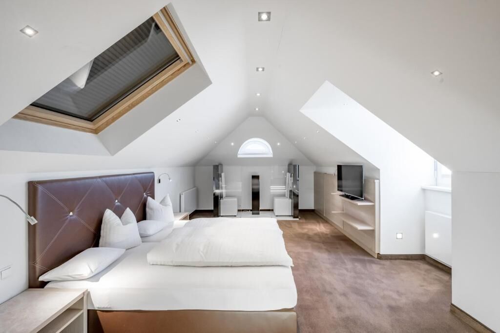 A modern bedroom with a large bed, a skylight, a TV, and a bathroom.
