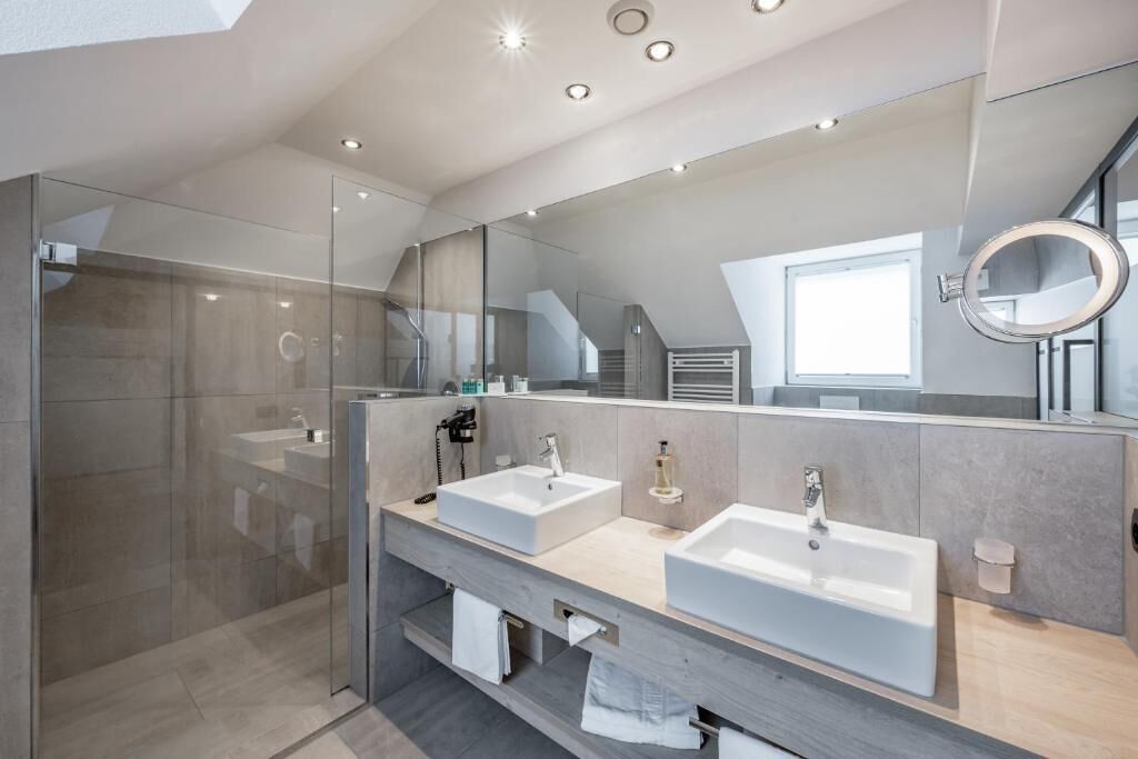 A modern bathroom with two sinks, a glass shower enclosure, and a large mirror.