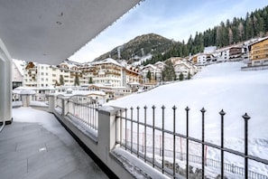 A snow-covered balcony with a view of a mountain and residential buildings. - Hotel Garni Christine - Ischgl (Ischgl)