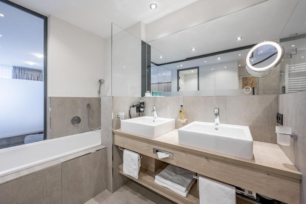 A modern bathroom with two sinks, a large mirror, and a bathtub.