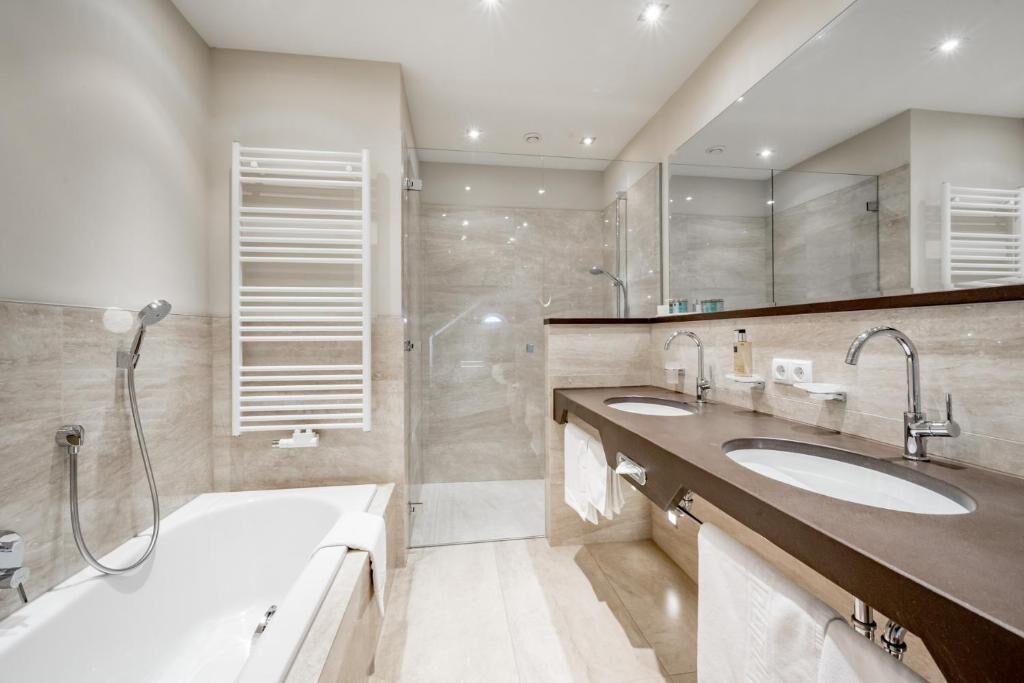 Ein modernes Badezimmer mit Badewanne, zwei Waschbecken, einer Dusche und einem großen Spiegel.